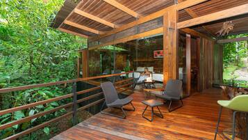An outdoor wooden deck with seating, surrounded by lush greenery.