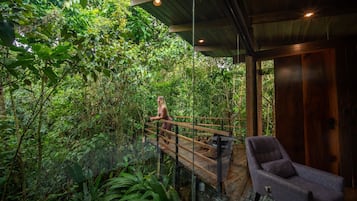 A wooden deck with a person walking, surrounded by dense greenery.