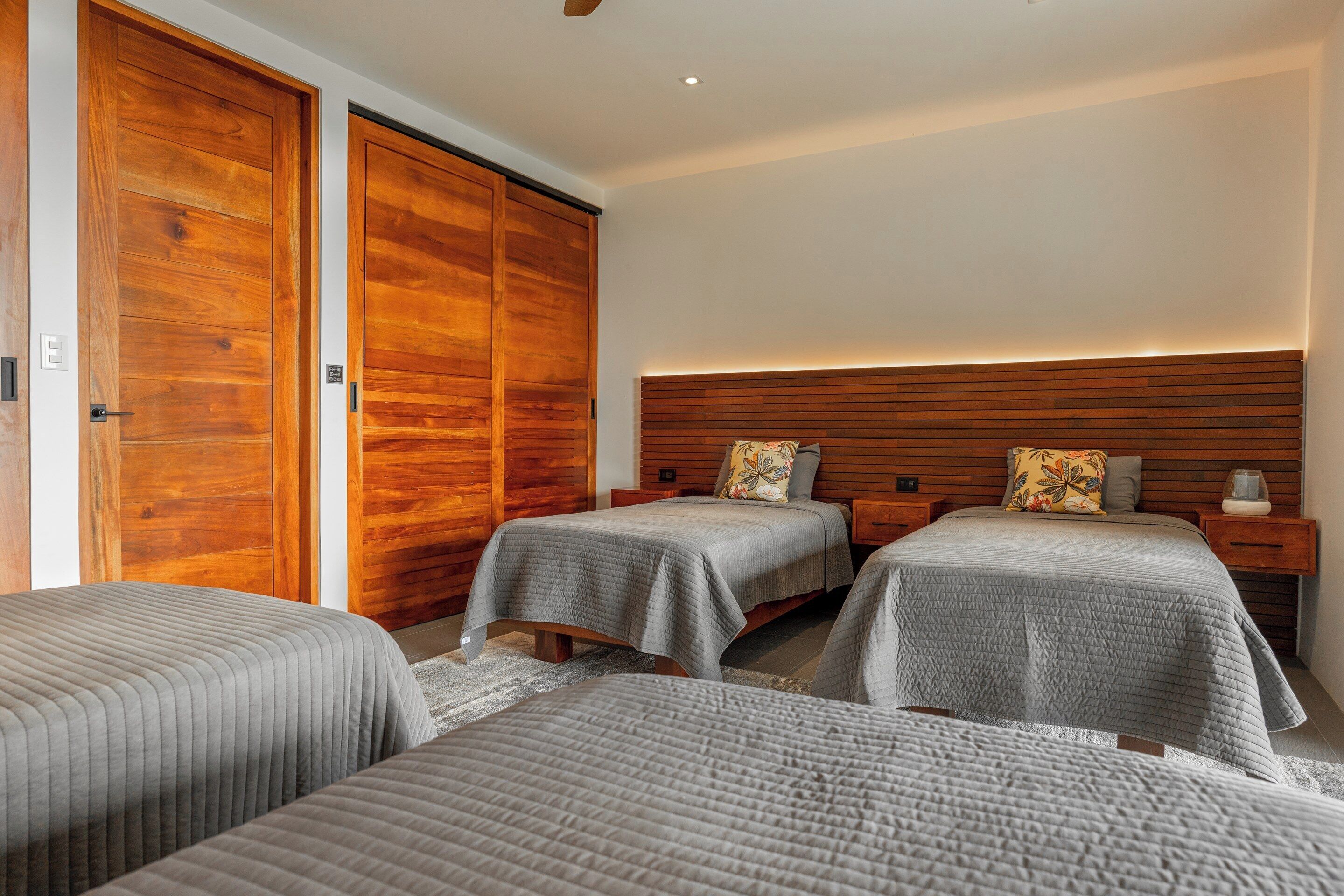 A bedroom with two beds, wooden wardrobes, and a headboard with built-in lighting.