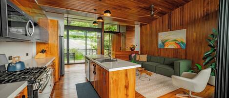 Una cocina moderna con armarios de madera, una isla central y un área de comedor con sofá verde y silla blanca.