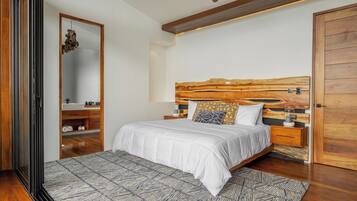 A modern bedroom with a wooden headboard, a large mirror, a bed with white bedding, and a patterned rug.