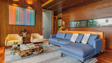A modern living room with a blue sofa, two armchairs, a coffee table with books and a plant, and a large abstract painting.