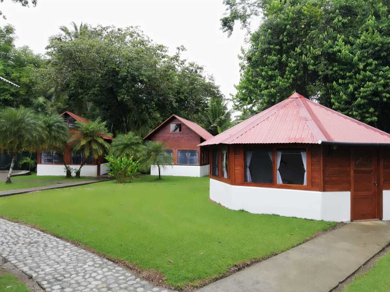 Un bungalow avec un toit rouge, entouré d’une pelouse bien entretenue et d’arbres.
