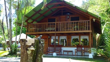 Surrounded by lush greenery, this cabin features a balcony with a bench and table.