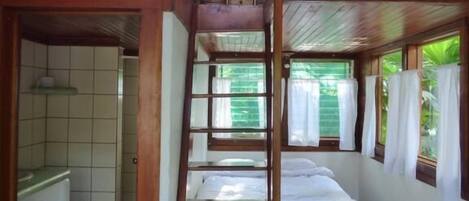 A room with a wooden ceiling, a bunk bed, a bathroom with a toilet, and a window with curtains.