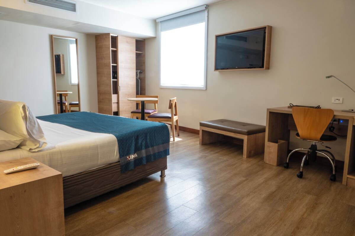 Ein Hotelzimmer mit Bett, Schreibtisch, Stuhl und Fernseher an der Wand.