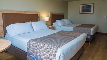 Quarto de hotel com duas camas, cada uma com cabeceira, mesa de cabeceira com abajur e um quadro na parede.