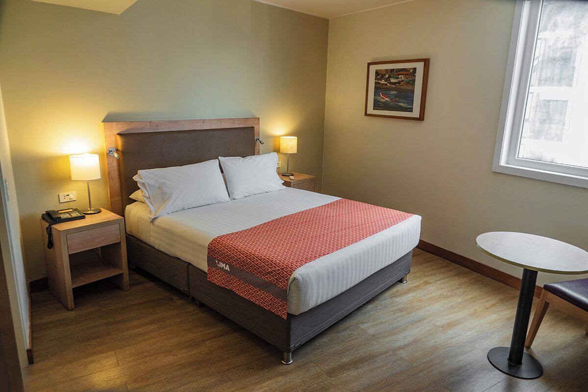 Ein Hotelzimmer mit Bett, Nachttischen, einem kleinen Tisch und einem Fenster.
