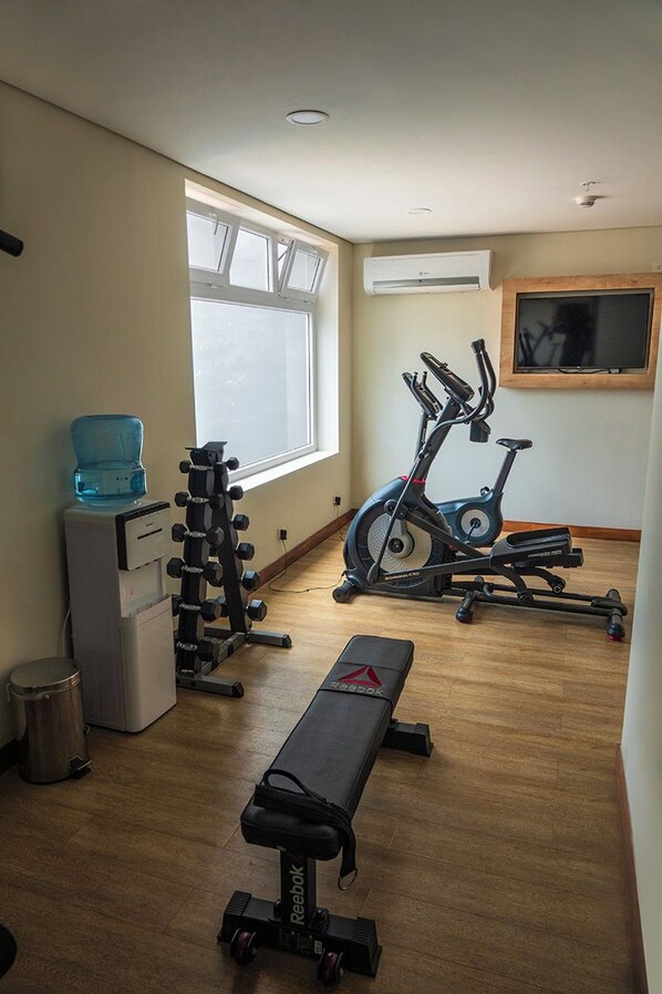 A gym with a bench, dumbbells, an exercise bike, and a water dispenser.