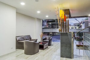 A modern living room with a leather sofa, a coffee table, and a vase of flowers. A staircase leads to an outdoor area with a view of buildings.