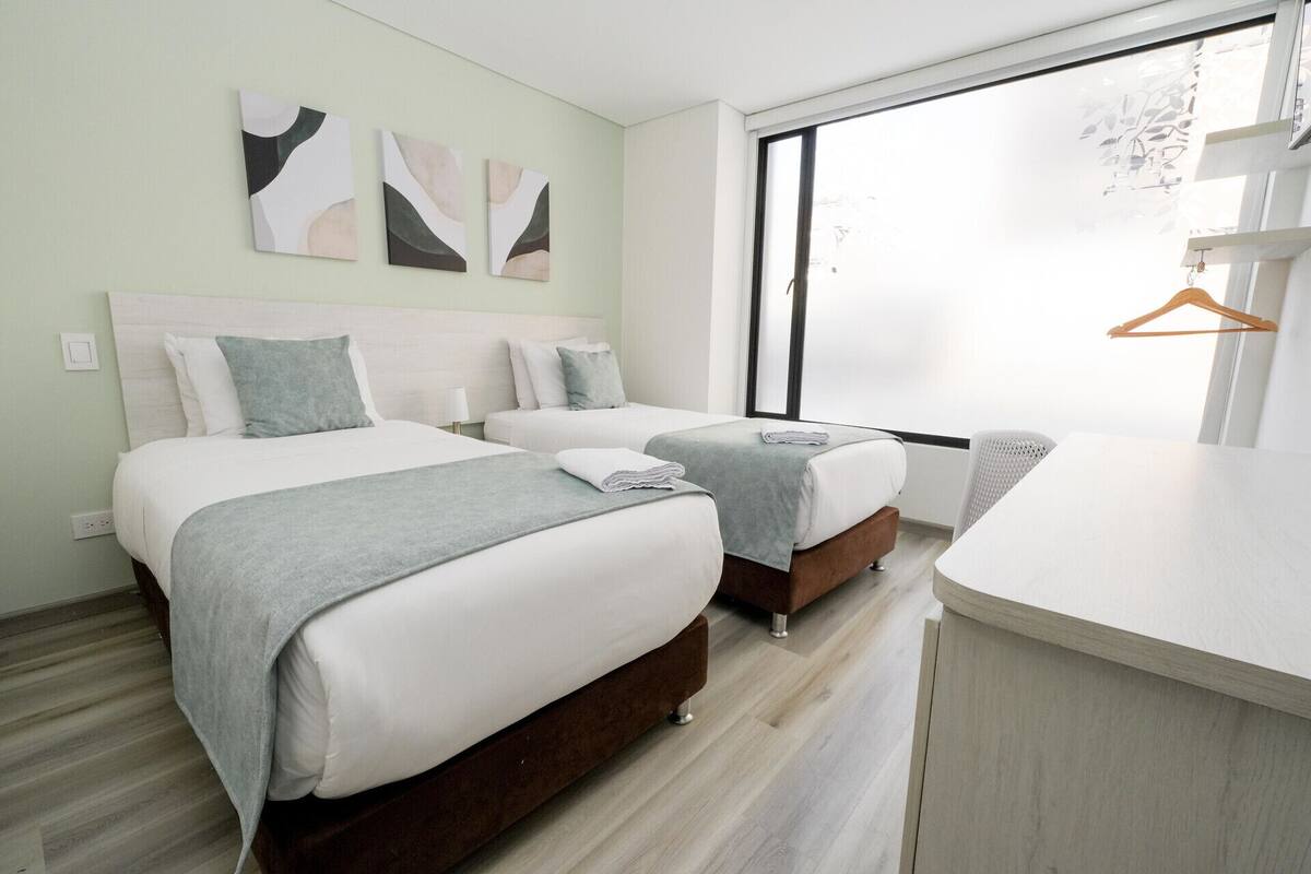 A hotel room with two beds, a large window, and a wooden floor.