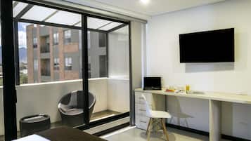 Un dormitorio moderno con un ventanal grande, un escritorio con una computadora portátil y un televisor en la pared.