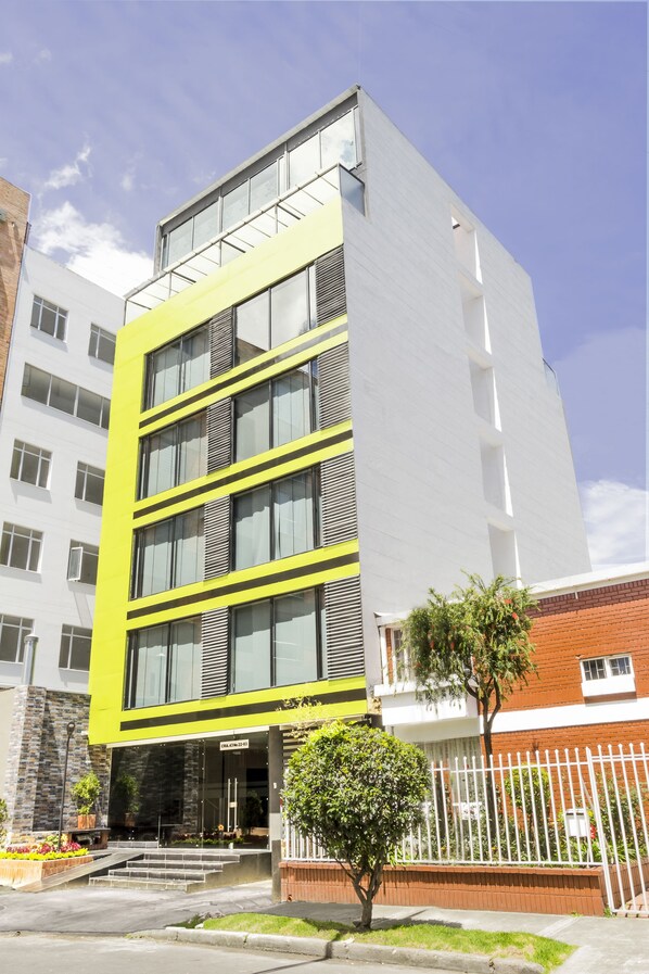 A modern building with a yellow facade, multiple windows, and a visible entrance with steps. - Hotel Regency Boutique La Feria (Bogotá)