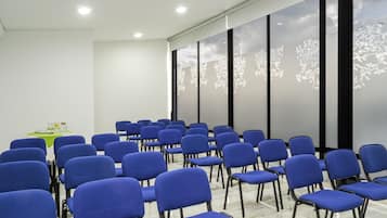 A conference room with rows of blue chairs, a projector screen, and a table with a green tablecloth.