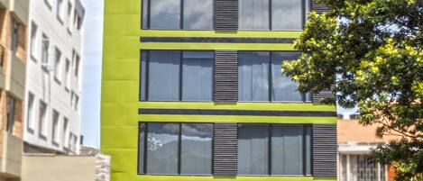 A modern building with a green facade, multiple windows, and a gated entrance.
