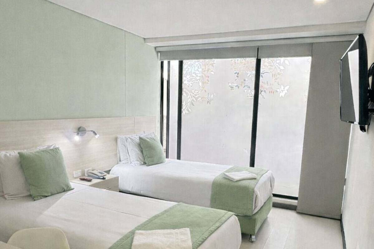 A modern hotel room with two beds, a desk, and a large window.