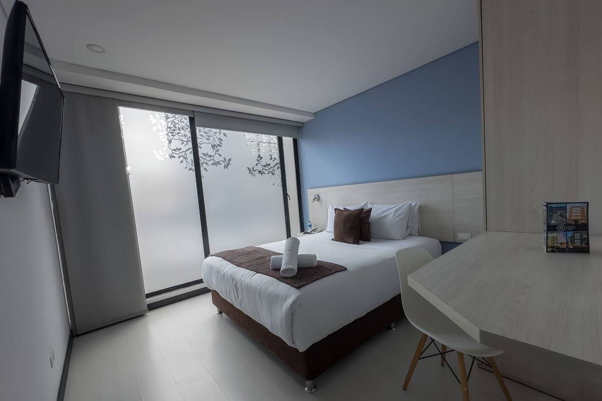 A modern hotel room with a bed, bedside table, and a large window.