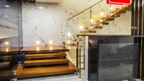 Una escalera moderna con escalones de madera y barandillas de vidrio, que conduce a una pared de tonos oscuros.