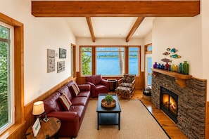Una sala de estar acogedora con chimenea, sofá de cuero y vista al lago.