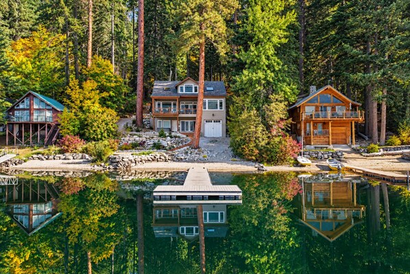 A lakeside property with multiple cabins, a dock, and a reflection in the water.