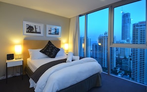 Relax in a spacious room with a large bed, framed photographs, and a nightstand, offering a panoramic city view.