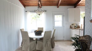 Un comedor con una mesa redonda, cuatro sillas, una araña y una cocina al fondo.