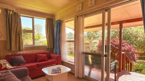 Una sala de estar con un sofá rojo, una mesa de centro blanca y un patio con puerta corrediza de vidrio.