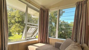 Una habitación con asiento junto a la ventana, cortinas y vistas al verde exterior.