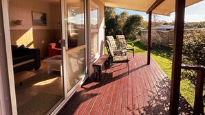 Una terraza cubierta con mobiliario exterior, una puerta corrediza de vidrio que da a un espacio interior con un sofá y una mesa de centro.