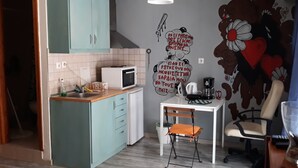 A compact kitchen with teal cabinets, a white countertop, a microwave, and a small dining table with a chair. There is a wall decoration with text and flowers. - The bohemian studio by the center (Thessaloniki)