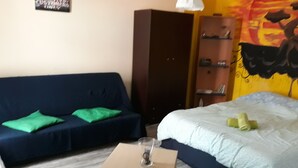 A room with a bed, a blue sofa with green cushions, a small table with a glass, a wardrobe, and a wall with a painting. - The bohemian studio by the center (Thessaloniki)