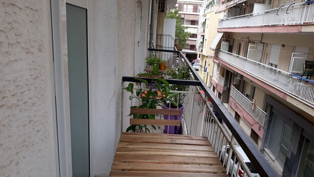 A narrow balcony with a wooden bench, potted plants, and a view of adjacent buildings. - The bohemian studio by the center (Thessaloniki)
