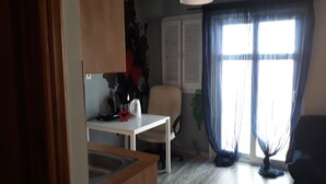 A modern kitchen with a white countertop, a coffee maker, and a red heart-shaped object. There is a dining table with a chair, a window with curtains, and a hanging plant. - The bohemian studio by the center (Thessaloniki)