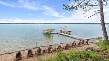 Relax by the serene lake with a boat moored at the dock, surrounded by a tranquil landscape and comfortable Adirondack chairs.