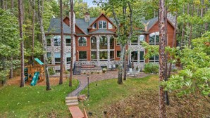 A large, two-story house surrounded by tall trees, with a stone exterior and large windows.