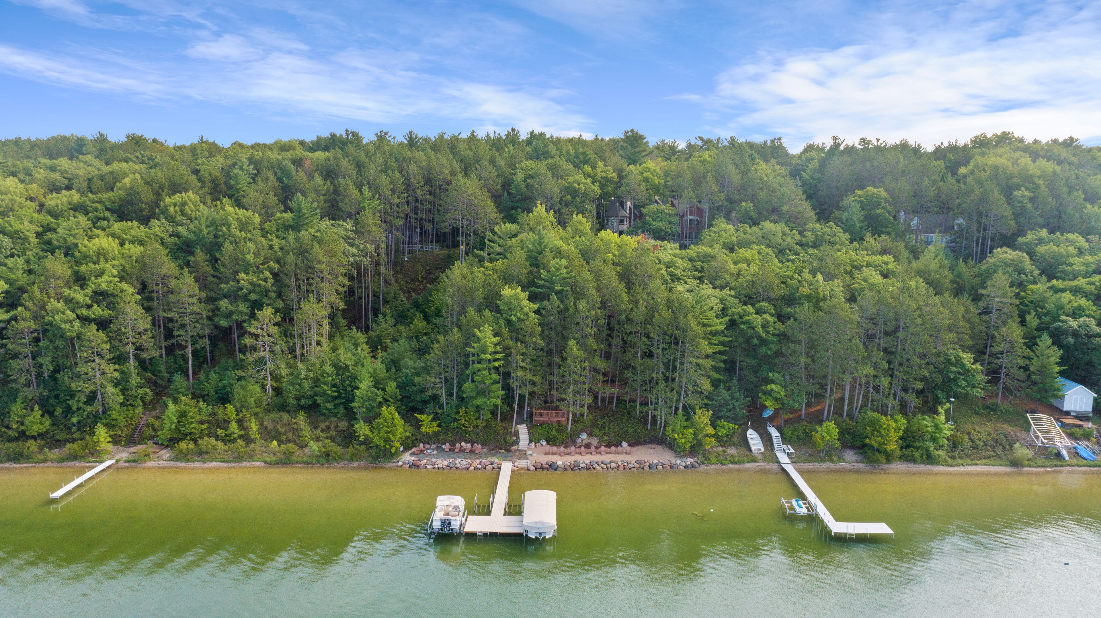 Une propriété au bord du lac, avec des bateaux amarrés, une terrasse en bois et une colline boisée.