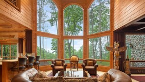 A spacious room with large windows, a wooden ceiling, leather furniture, and a stone wall.