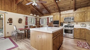 Una cocina con armarios de madera, una isla central, un microondas, un horno y una zona de comedor con una mesa y sillas.