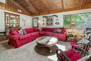 A cozy living room with a red sectional sofa, a wooden coffee table, and a large window with a view of trees.