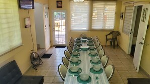 A dining area with a long table set for a meal, chairs, a fan, and a door leading outside.