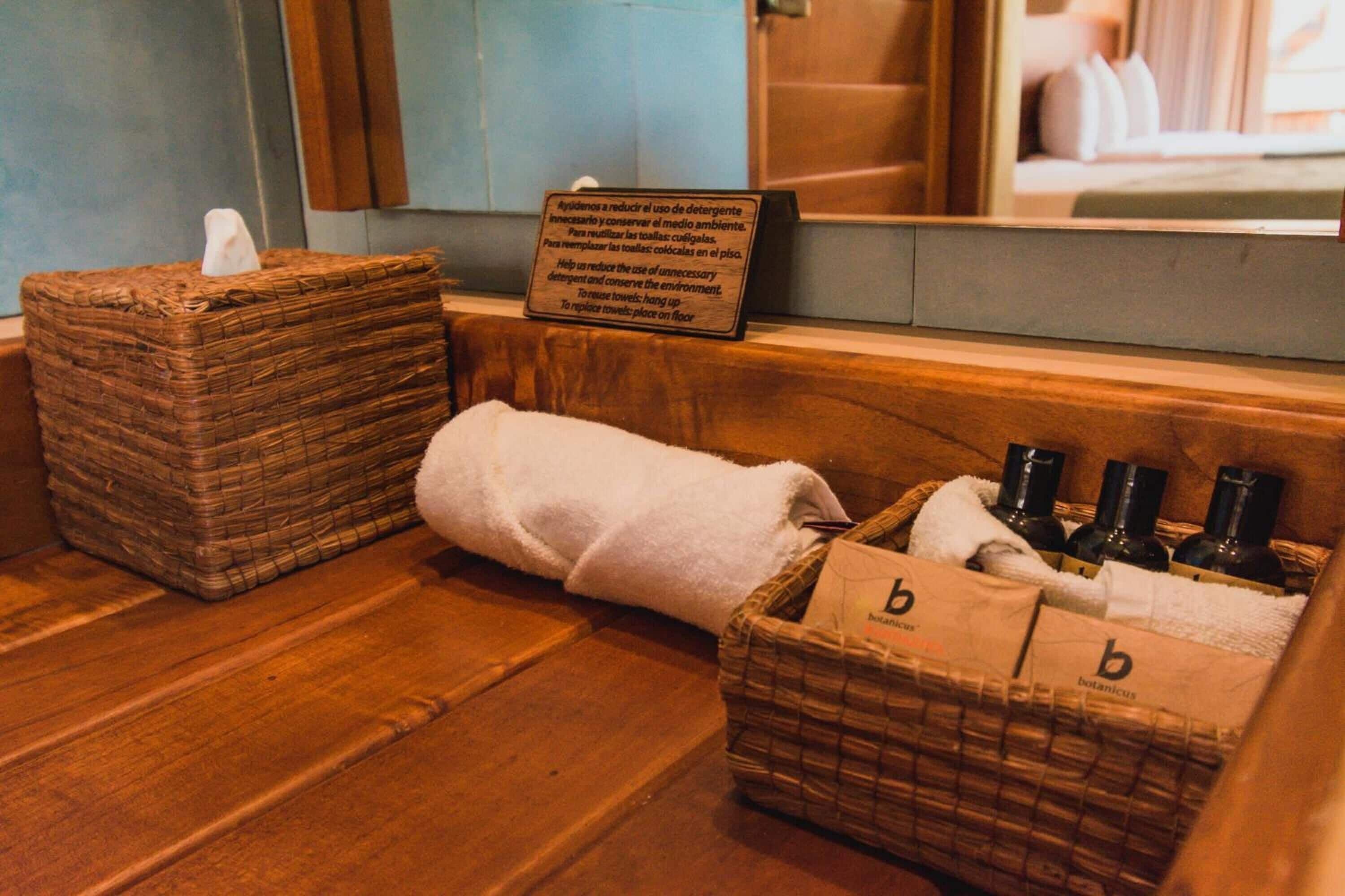 A bathroom with a wooden floor, a white towel, and a basket containing bottles and a tissue box.