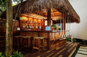 Eine Holztresne mit einem Reetdach, Barhocker und ein Schild, das einen Minibar-Service anzeigt.