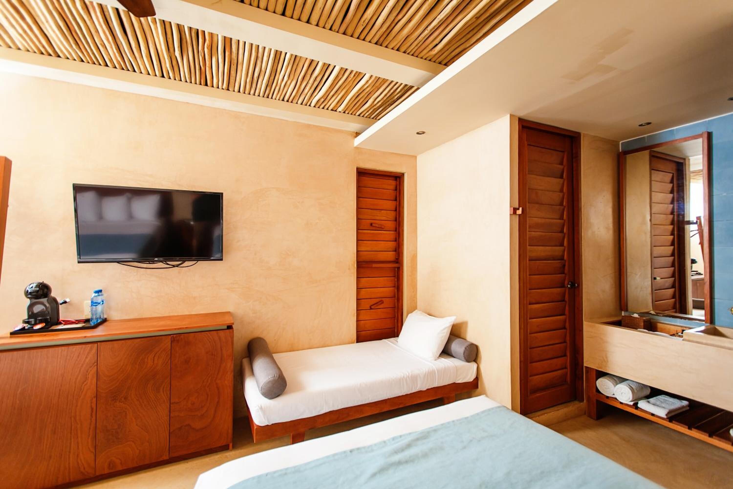 Un dormitorio con cama, televisor, armario de madera, un escritorio pequeño y baño con espejo.