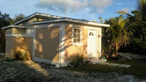 A single-story house with a flat roof, a small front porch, and a visible garage door. - The Colonial Rental Suite, Moss Town Exuma (Moss Town)