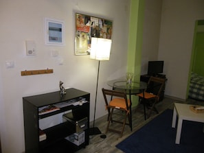 En hyggelig og kompakt indretning med et rundt bord, to stole, et skrivebord med stol, et fjernsyn og en lampe.