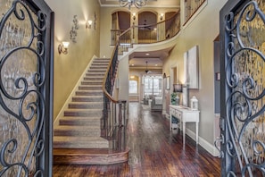 A grand staircase with a wooden handrail and black metal balusters, leading to a second-floor landing with a balcony.