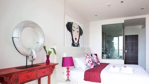 Een moderne slaapkamer met een bed, een rode console tafel, een spiegel en een schilderij aan de muur.