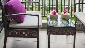 Een balkon met rieten meubilair, een glazen tafel en twee decoratieve objecten.