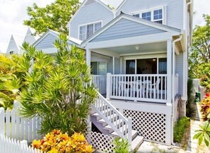 Ein zweistöckiges Haus mit Veranda, Garage und einem kleinen Garten mit tropischen Pflanzen.