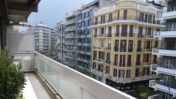 A balcony with a view of multi-story buildings, including a yellow building with red shutters. - Luxury in the heart of the city (Thessaloniki)